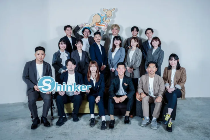 株式会社Shinkerのロゴボードを持つスタッフを中心に、社員十数名が並んだ集合写真